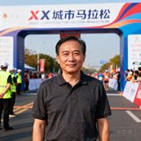 城市马拉松赛事总监李明辉先生近照，身穿深色polo衫站在赛事终点拱门前